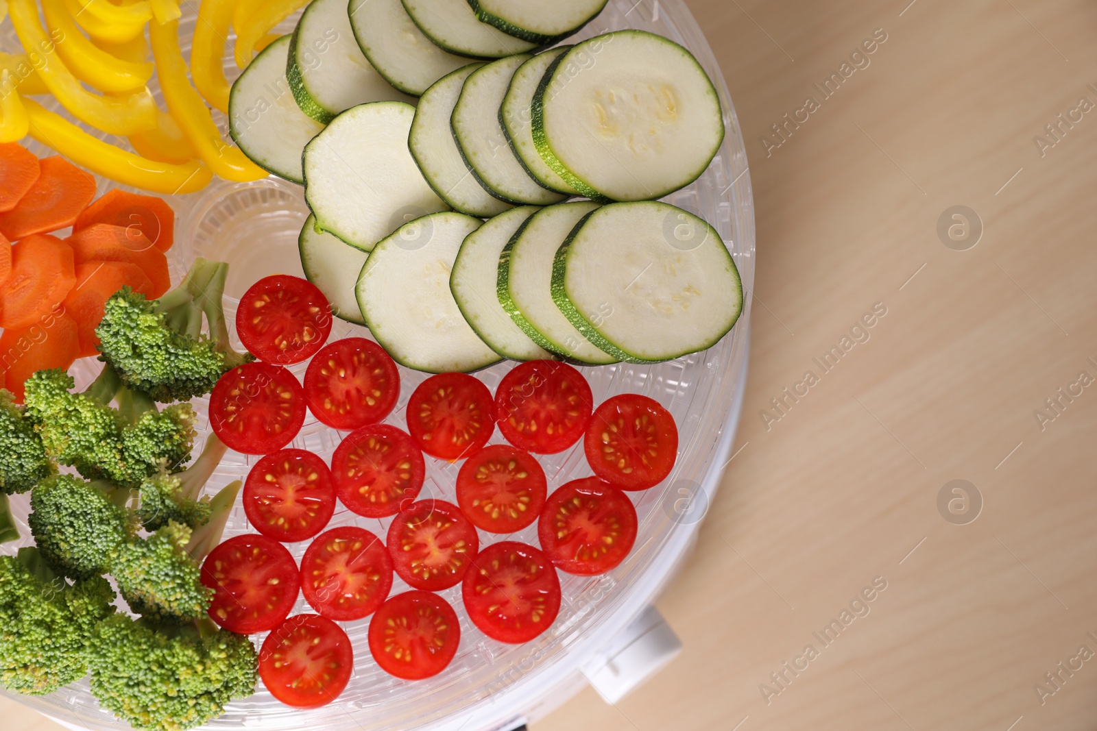 Photo of Cut vegetables in fruit dehydrator machine on wooden table, top view