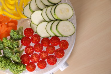 Cut vegetables in fruit dehydrator machine on wooden table, top view