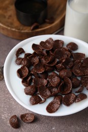 Photo of Breakfast cereal. Chocolate corn flakes and milk in bowl on brown table, closeup