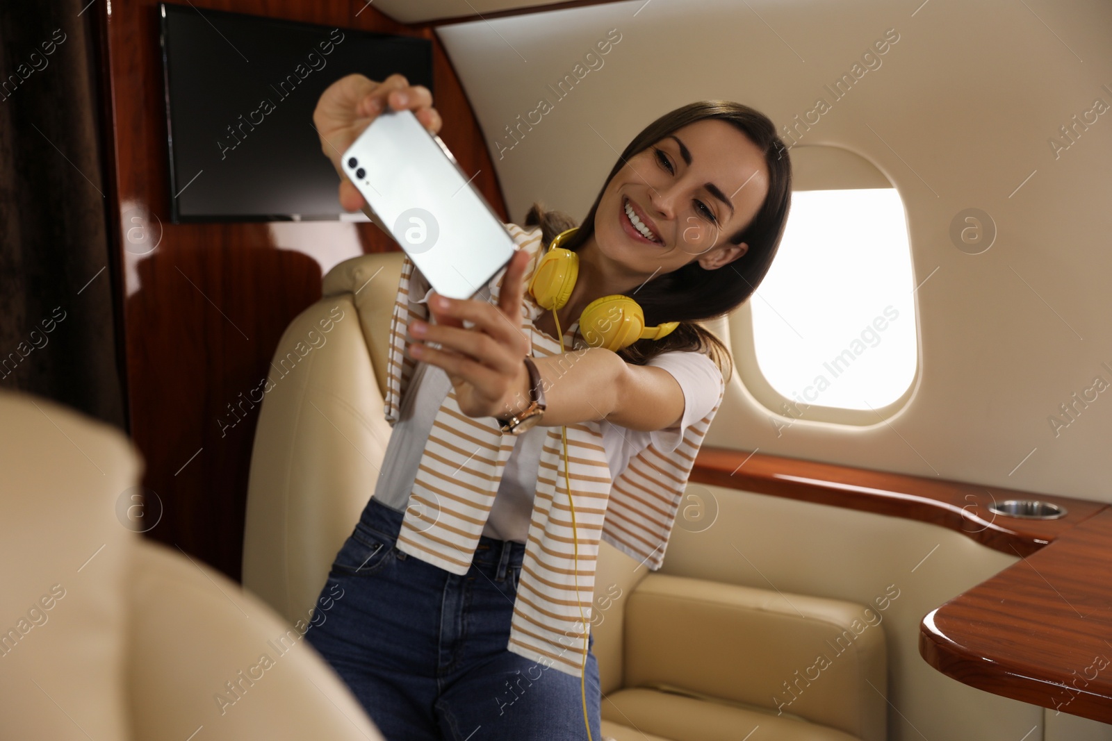 Photo of Young woman with headphones taking selfie in airplane during flight