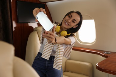 Photo of Young woman with headphones taking selfie in airplane during flight