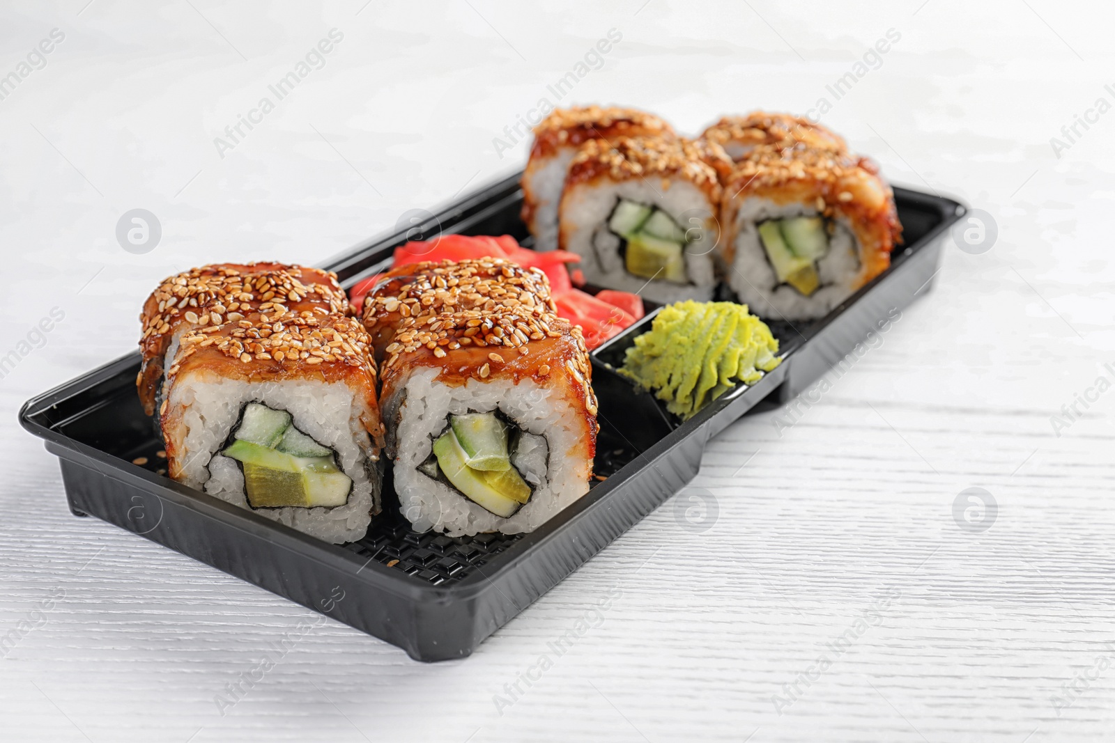 Photo of Box with tasty sushi rolls on white table. Food delivery