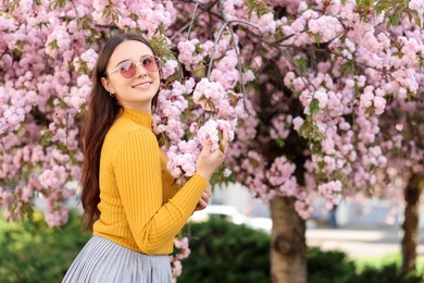 Beautiful woman in sunglasses near blossoming tree on spring day