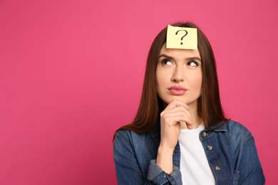 Photo of Pensive woman with question mark sticker on forehead against pink background. Space for text