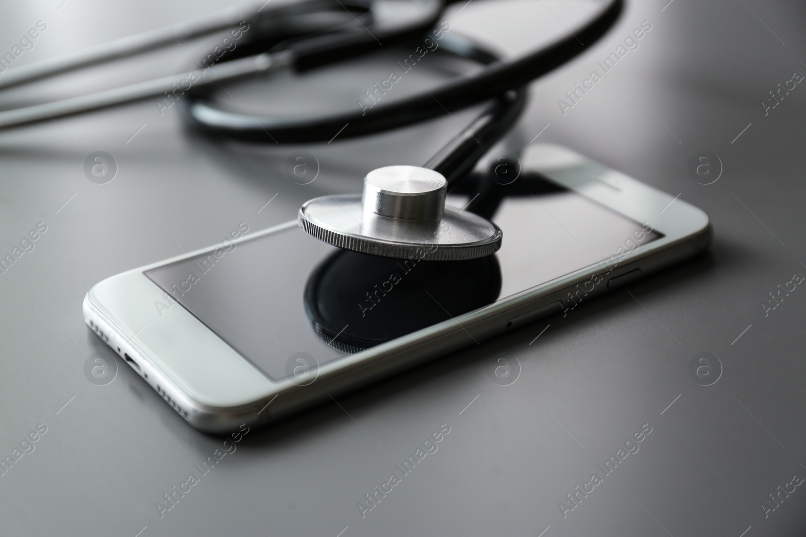 Photo of Smartphone and stethoscope on grey table, closeup. Repairing service