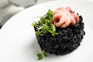 Photo of Delicious black risotto with baby octopus in plate, closeup