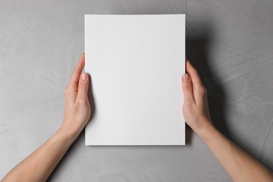 Woman holding notebook with blank cover at light grey table, top view. Mockup for design