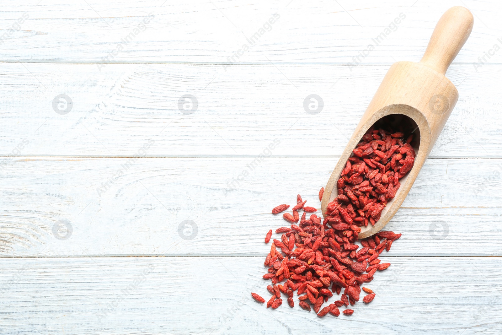 Photo of Scoop and dried goji berries on white wooden table, top view with space for text. Healthy superfood