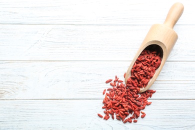 Scoop and dried goji berries on white wooden table, top view with space for text. Healthy superfood