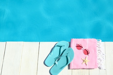 Beach accessories on wooden deck near swimming pool. Space for text