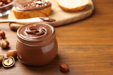 Glass jar with tasty chocolate hazelnut spread and nuts on wooden table. Space for text