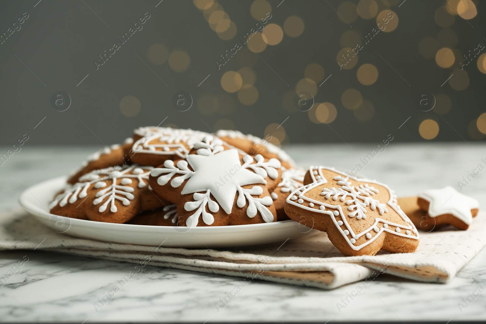 Photo of Tasty Christmas cookies with icing on white marble table against blurred lights