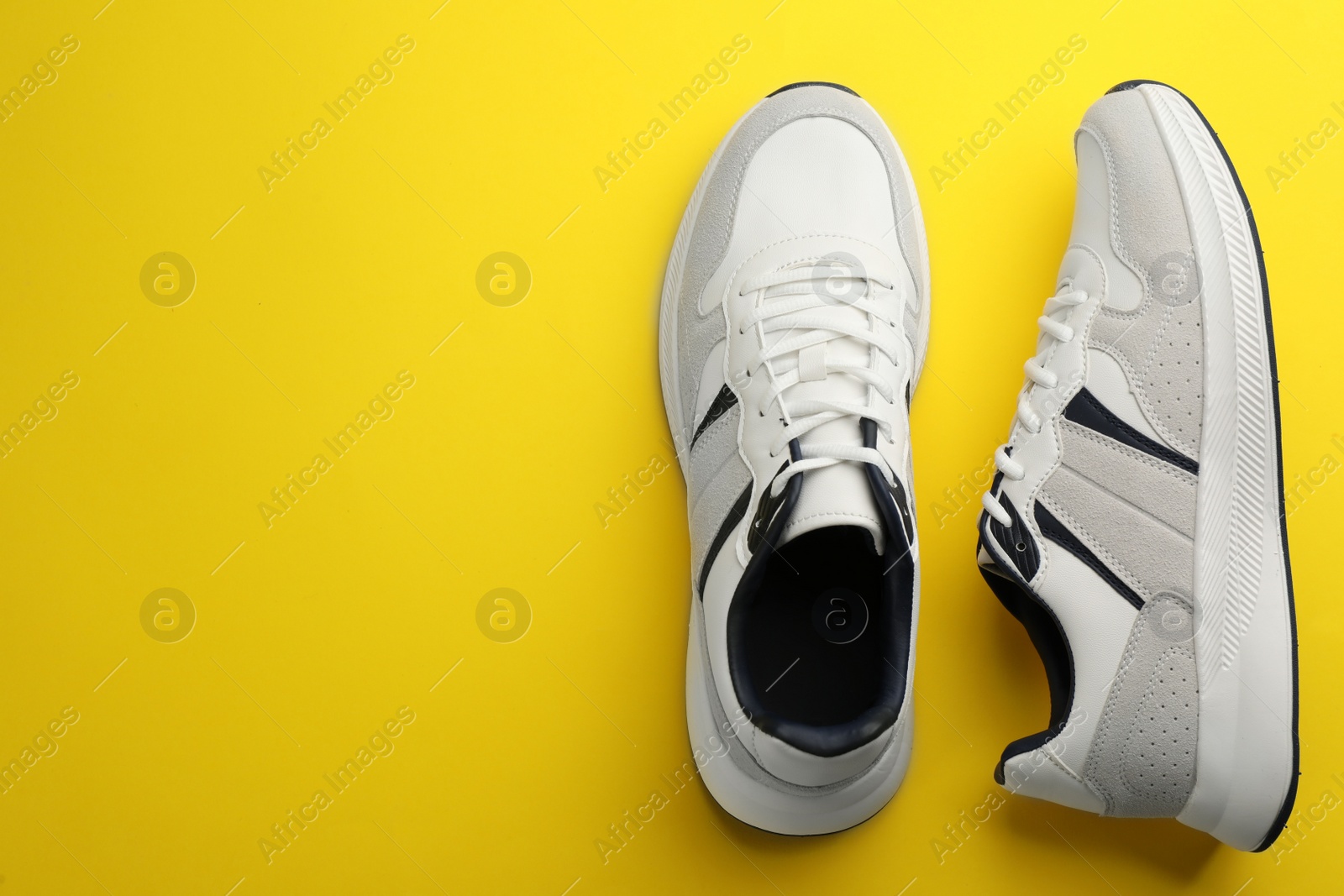 Photo of Pair of stylish sports shoes on yellow background, flat lay. Space for text