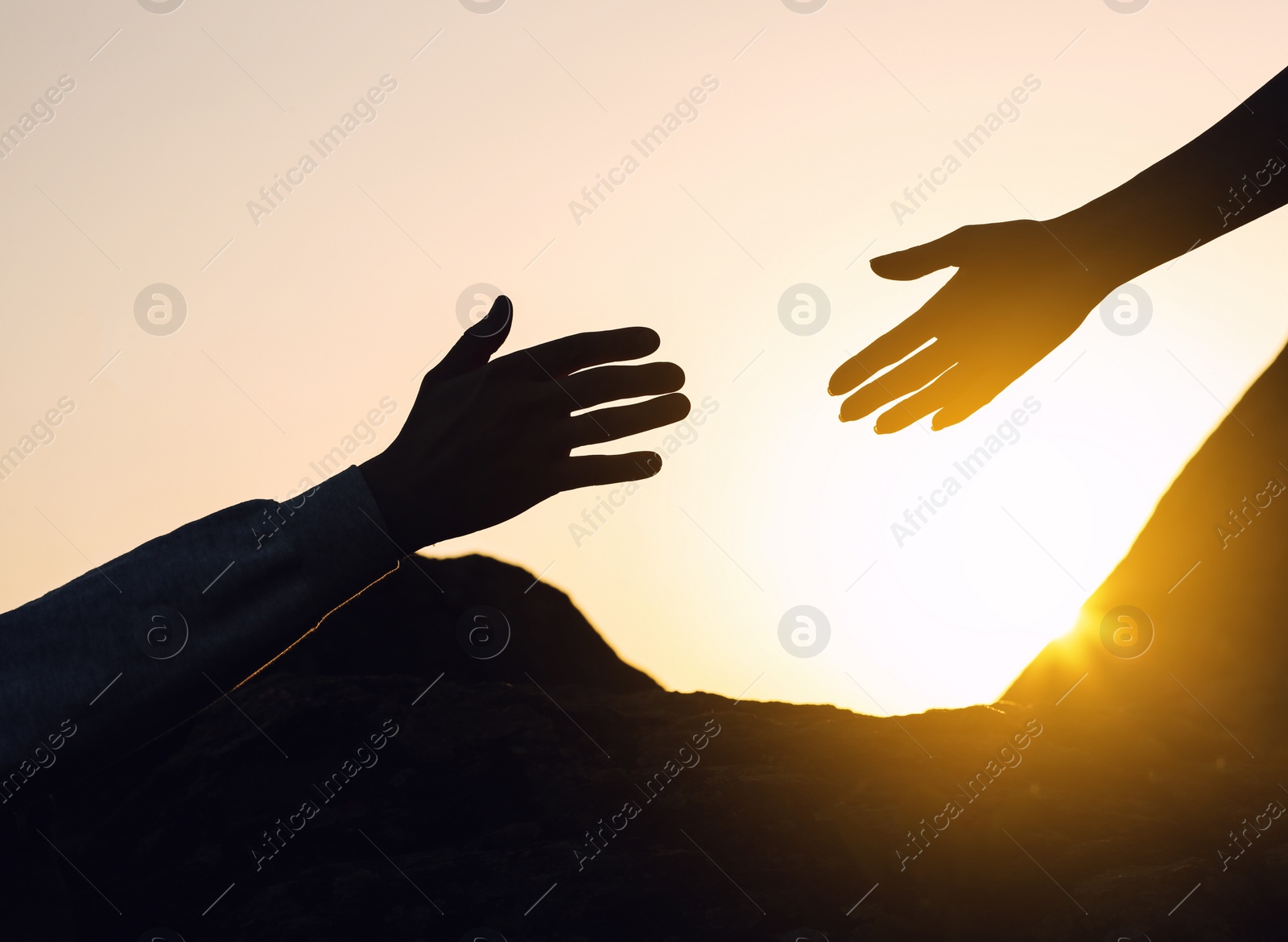 Photo of Silhouettes of man and woman helping each other to climb on hill against sunset, closeup