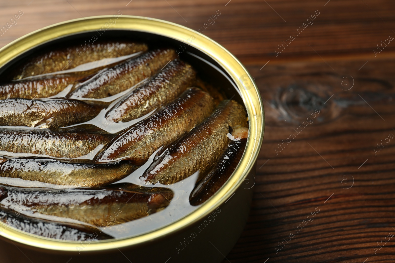 Photo of Open tin can of sprats on wooden table, closeup