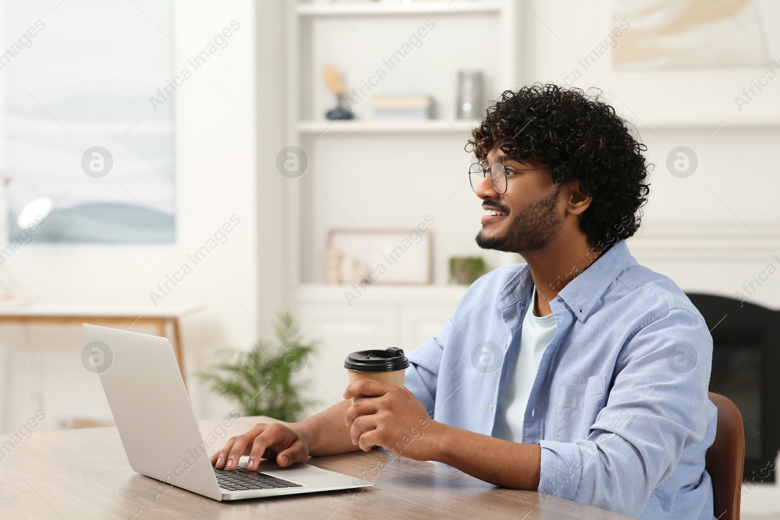 Photo of Handsome smiling man with coffee using laptop in room