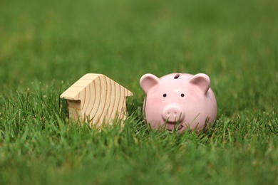 Photo of Piggy bank and model of house in green grass outdoors