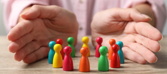 Image of Woman protecting colorful pawns at wooden table, closeup. Diversity and Inclusion concept