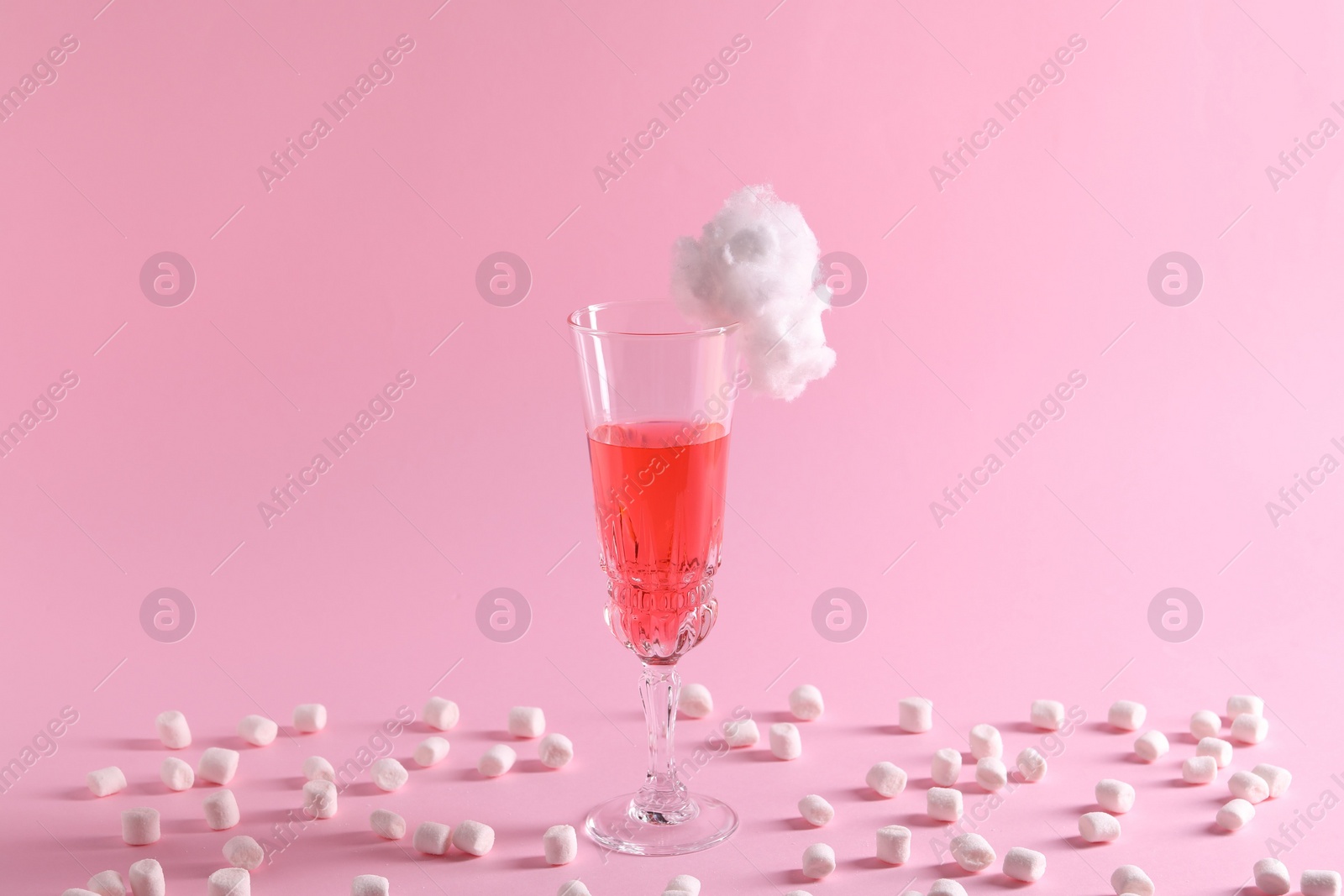 Photo of Tasty cocktail in glass decorated with cotton candy and marshmallows on pink background