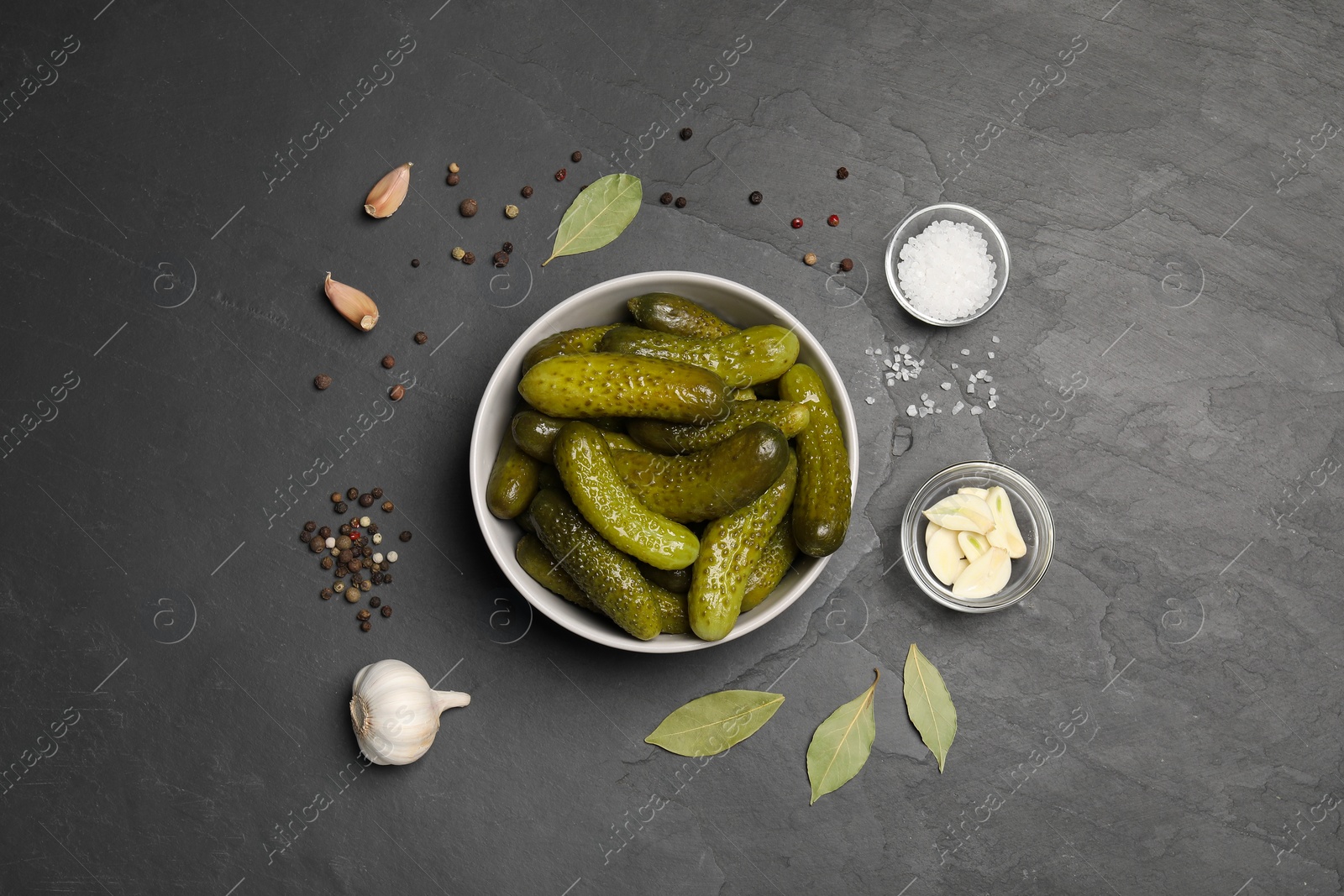 Photo of Tasty pickled cucumbers in bowl and spices on grey textured table, flat lay