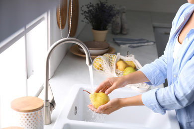 Photo of Woman washing fresh ripe pear in kitchen, closeup