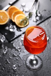 Photo of Glass of tasty Aperol spritz cocktail with orange slices and ice cubes on dark gray table, above view