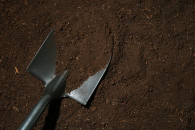 Photo of Metal shovel on fertile soil, top view and space for text. Gardening tool