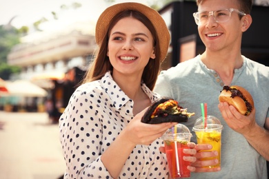 Photo of Young happy couple with burgers walking on city street