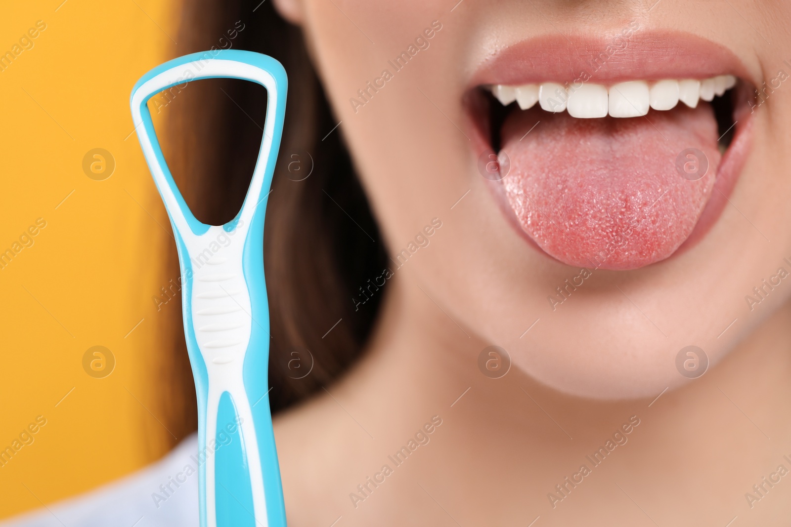 Photo of Woman brushing her tongue with cleaner on yellow background, closeup