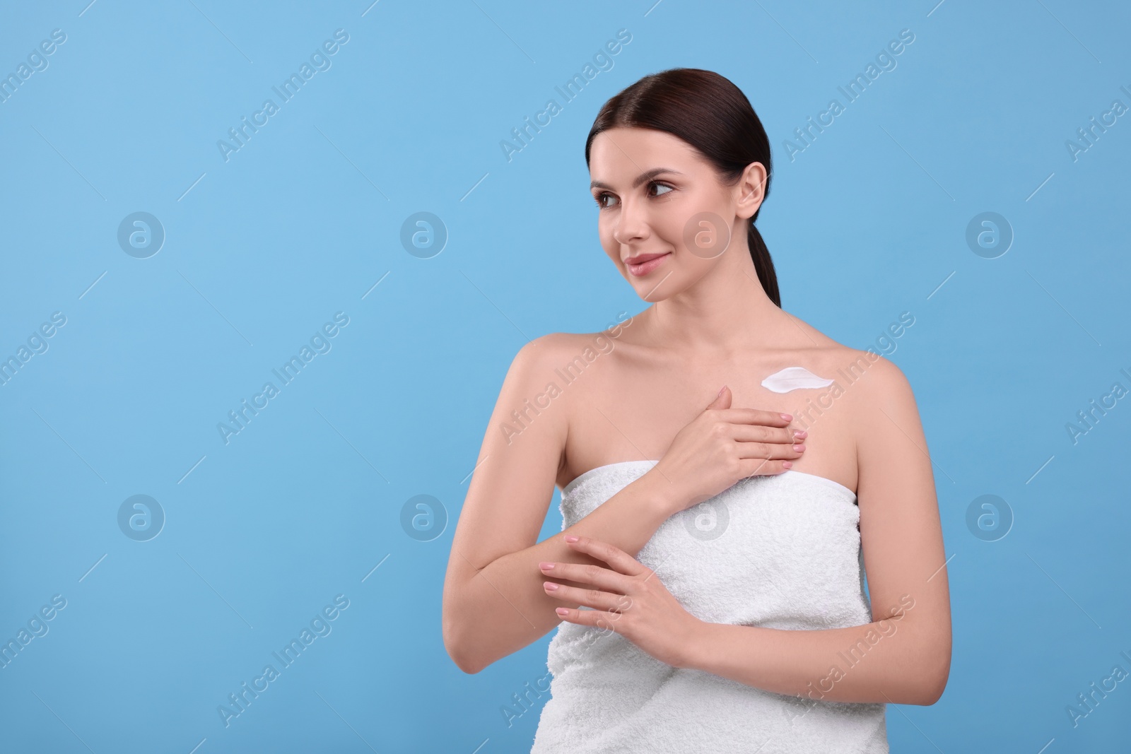 Photo of Beautiful woman with smear of body cream on light blue background, space for text