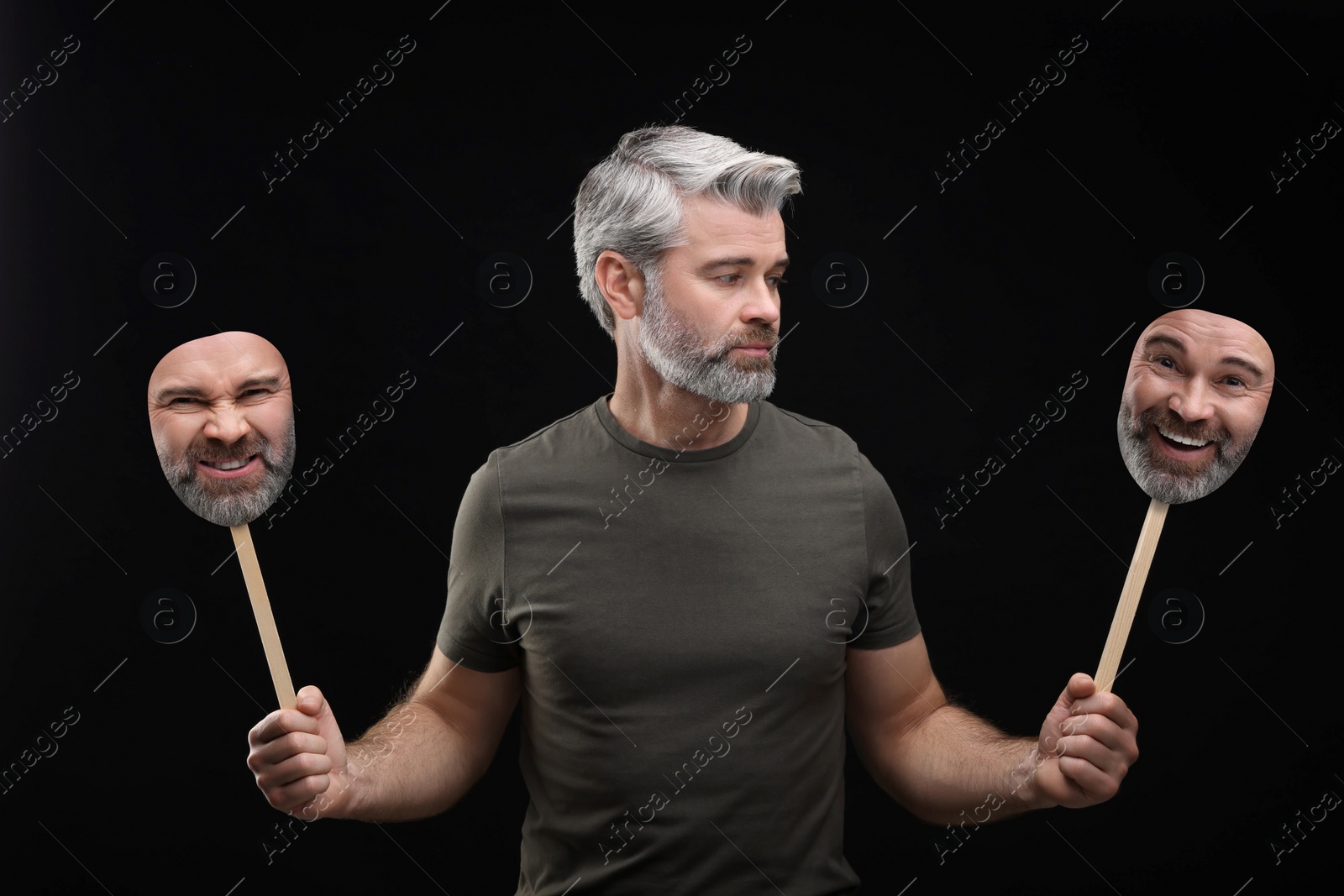 Image of Mature man holding masks with his face showing different emotions on black background. Balanced personality