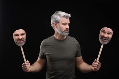 Mature man holding masks with his face showing different emotions on black background. Balanced personality