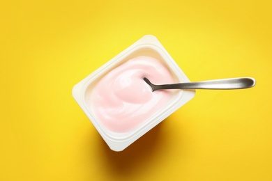 Photo of Plastic cup with creamy yogurt and spoon on color background, top view