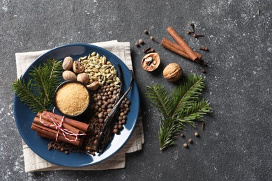 Different aromatic spices and fir branches on grey textured table, flat lay