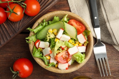 Photo of Crab stick salad with tomatoes and lettuce on wooden table, flat lay