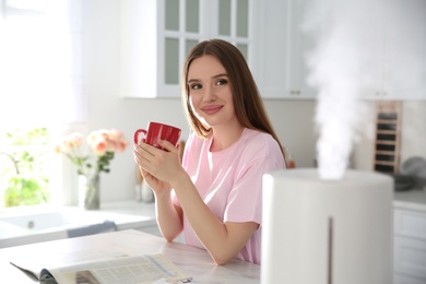Photo of Woman drinking coffee in kitchen with modern air humidifier