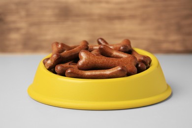 Photo of Yellow bowl with bone shaped dog cookies on light table, closeup