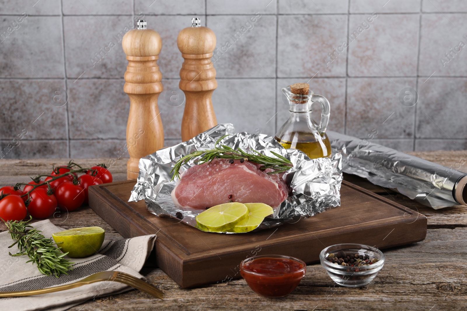 Photo of Aluminum foil with raw meat, rosemary, lime and spices on wooden table