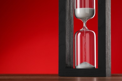 Photo of Hourglass with flowing sand on table against red background, space for text