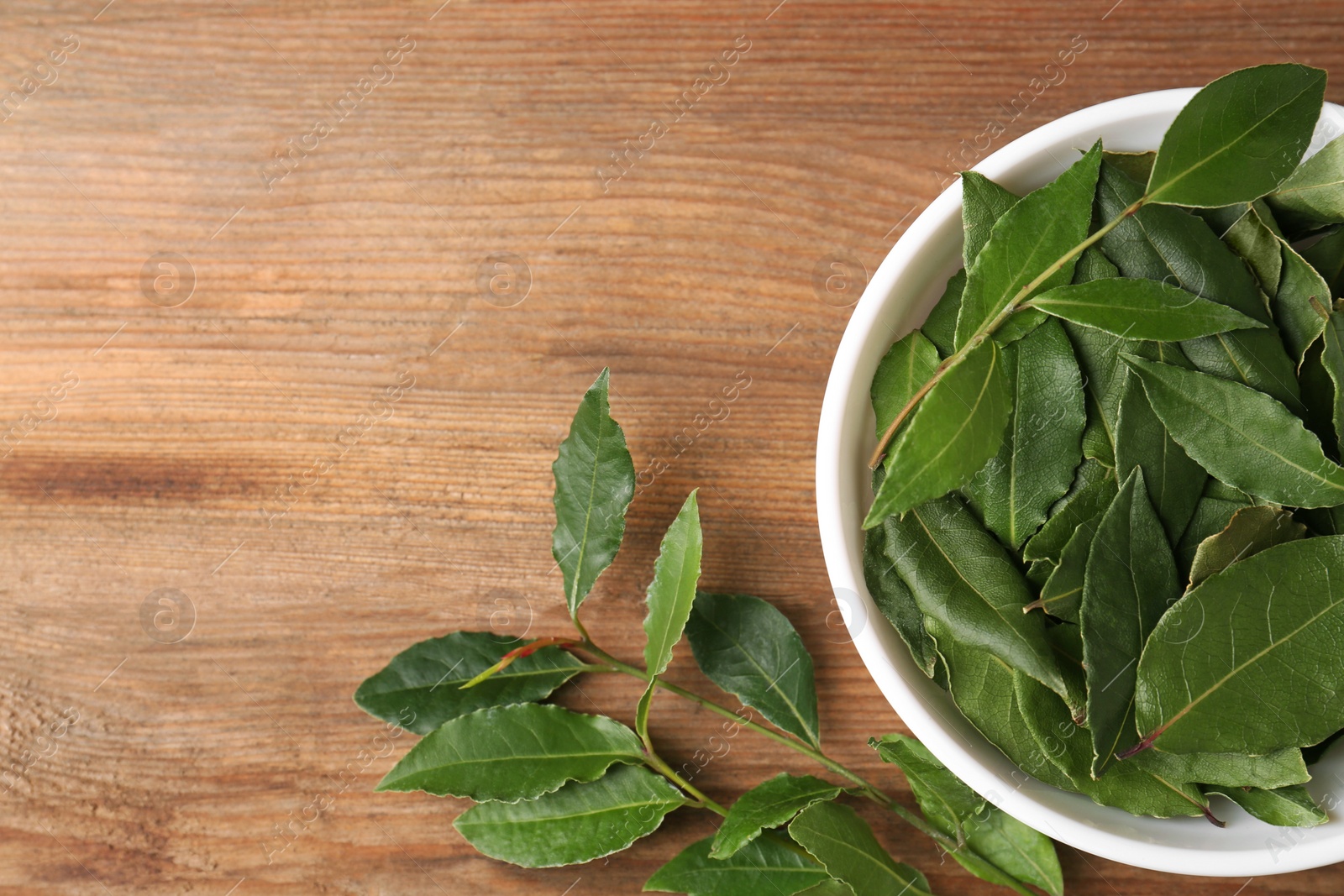 Photo of Aromatic fresh bay leaves and bowl on wooden table, flat lay. Space for text