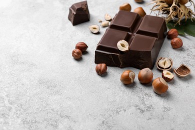 Photo of Delicious chocolate and hazelnuts on light table, space for text