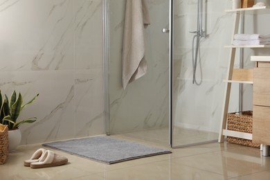 Soft grey bath mat and slippers on floor in bathroom