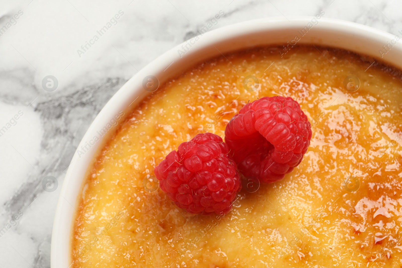 Photo of Delicious creme brulee with raspberries on white marble table, closeup