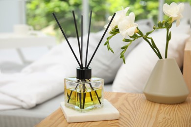 Reed diffuser and vase with bouquet on wooden nightstand in bedroom
