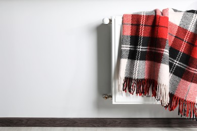 Photo of Checkered blanket hanging on white radiator indoors. Space for text