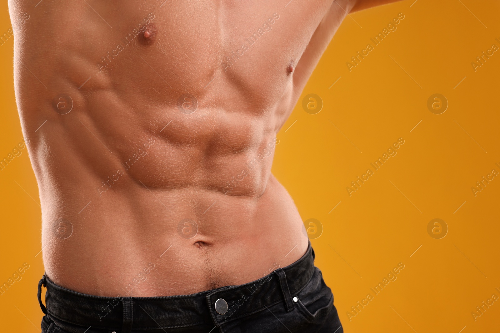 Photo of Muscular man showing abs on orange background, closeup. Sexy body