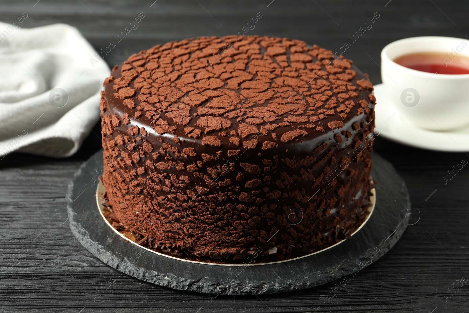 Photo of Delicious chocolate truffle cake and tea on black wooden table