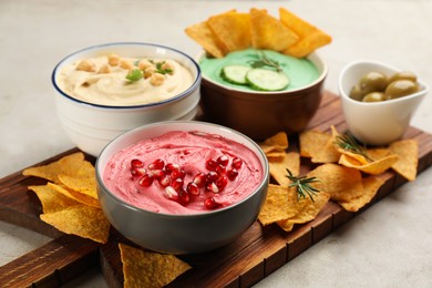 Photo of Different kinds of tasty hummus served with nachos on light table