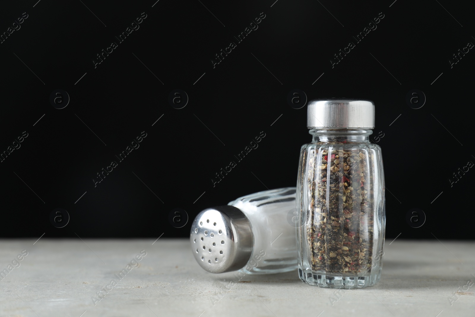 Photo of Salt and pepper shakers on light table against black background. Space for text