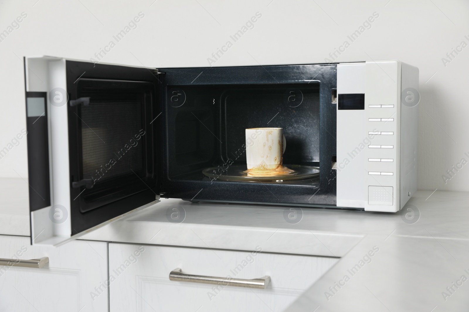 Photo of Dirty microwave oven with cup of coffee in kitchen